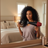 Woman using a hair dryer in front of a mirror in a bedroom.