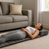 Woman lying on a gray massage mat in a living room.