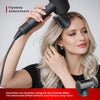 Woman using a hair dryer with a flyaway attachment on her hair against a plain background