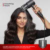 Woman using a hair dryer with a smoothing nozzle on her hair against a gray background